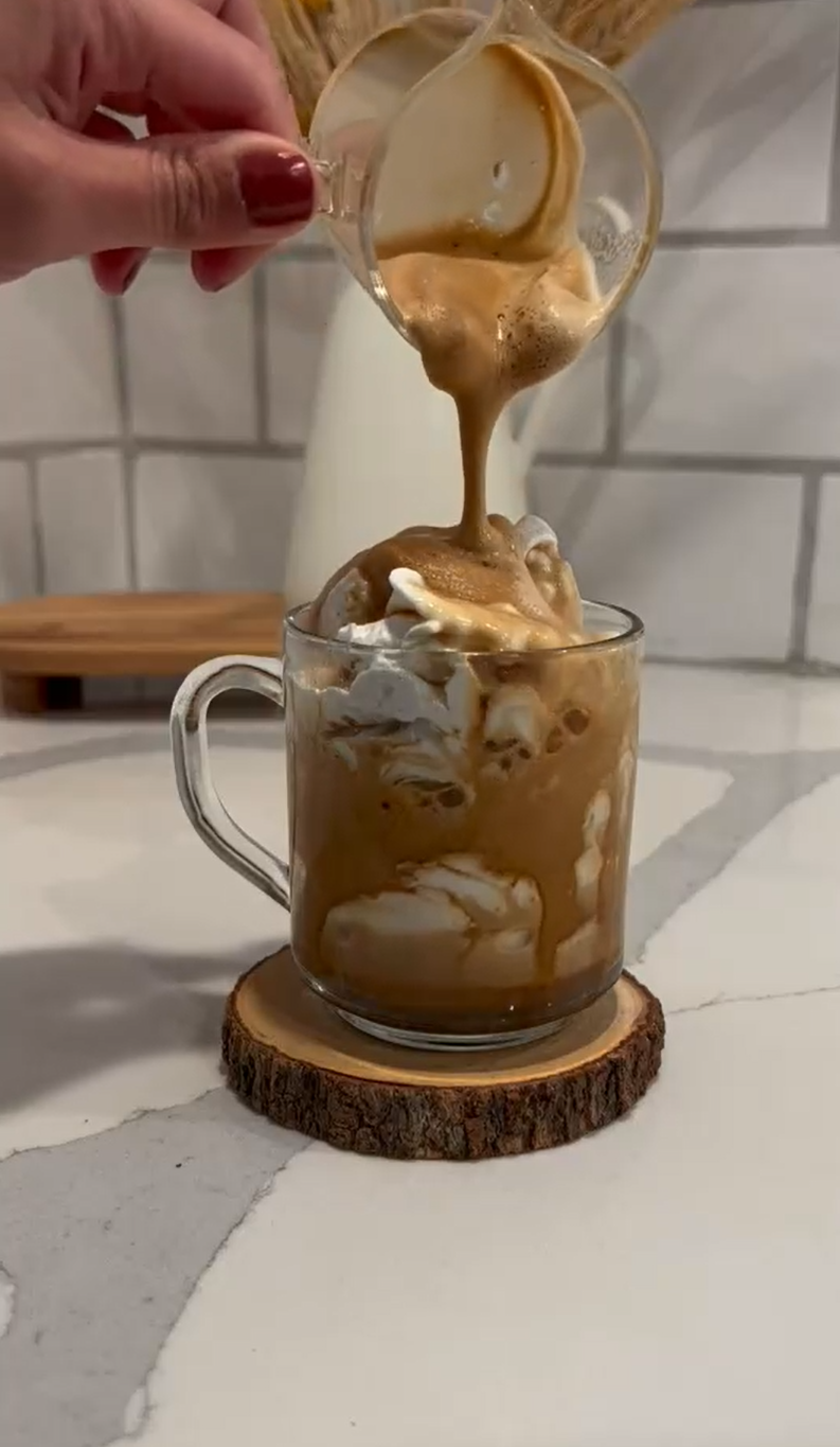 Pouring espresso over whipped cream in a glass mug