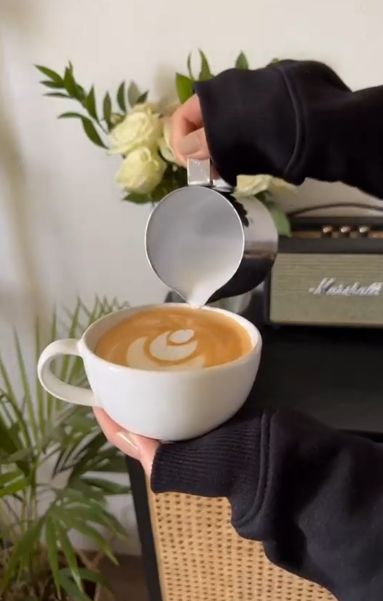 Pouring latte art into cappuccino with cream roses and a speaker